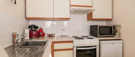 A compact kitchen with white cabinets, a stainless steel sink, a microwave, a stove, and a dishwasher.
