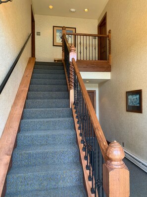 A staircase with a wooden handrail and black balusters, carpeted in blue with a textured pattern.