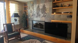 A living room with a fireplace, television, wooden shelves, and a Christmas tree. - Lakeside, Ski Condo with Amazing Views, Quiet, Family-Friendly (Keystone (Dillon))