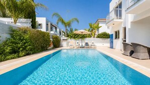 A swimming pool with lounge chairs, a pergola, and a white building with balconies. - Villa Marina - Three Bedroom Villa, Sleeps 6 (Pernera)