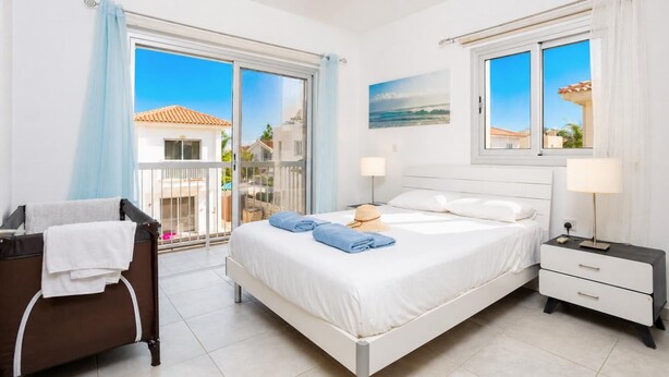 A bedroom with a bed, bedside tables, a desk, and a view of the outside. - Villa Marina - Three Bedroom Villa, Sleeps 6 (Pernera)