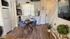A modern kitchen with a dining area, featuring a round table with chairs, a ceiling fan, and a TV mounted on the wall.