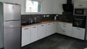 A kitchen with white cabinets, a stainless steel refrigerator, a microwave, and a window above the sink. - New single-storey house 800 metres from the sea and footpaths (Pleubian)