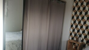 A bedroom with a bed, a wardrobe, a mirror, a curtain, and a patterned wall. - New single-storey house 800 metres from the sea and footpaths (Pleubian)