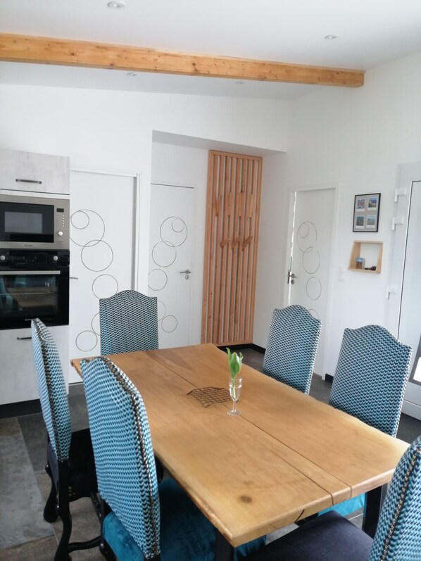 A dining area with a wooden table and blue patterned chairs, a built-in oven, and a wooden slat partition.