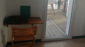 A room with a wooden chair, a small table, and a suitcase. There is a sliding glass door leading to an outdoor deck. - New single-storey house 800 metres from the sea and footpaths (Pleubian)