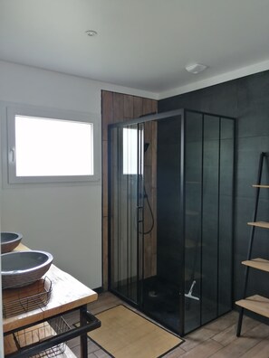 A modern bathroom with a glass shower enclosure, a wooden vanity with a sink, and a small window providing natural light.