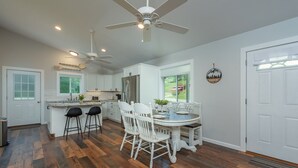 Een moderne keuken met witte kasten, een groot eiland met barstoelen, een eettafel met stoelen en een plafondventilator.