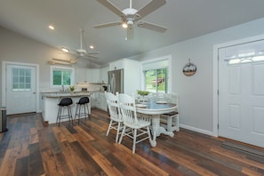 A modern kitchen with white cabinetry, a central island with bar stools, and a dining table with chairs.