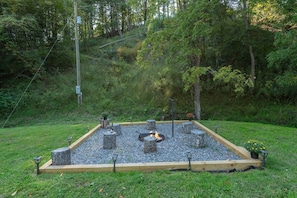 A fire pit surrounded by wooden posts and gravel, set in a garden with a wooden border and potted plants. - Cozy Cottage~Hot Tub+Fire Pit+Grill~WiFi~Near AVL! (Burnsville)