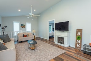 A spacious living room with a fireplace, a television, and a 'Welcome to Our Home' sign. - Cozy Cottage~Hot Tub+Fire Pit+Grill~WiFi~Near AVL! (Burnsville)