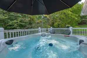 A hot tub with a waterfall feature, surrounded by a white deck and a black umbrella. - Hot Tub+Fire Pit, WiFi, Close to AVL+Burnsville! Perfect Location! Easy Access! (Burnsville)