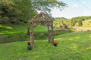 A rustic arbor structure in a grassy field with trees and a distant view of a hill. - Cozy Cottage~Hot Tub+Fire Pit+Grill~WiFi~Near AVL! (Burnsville)