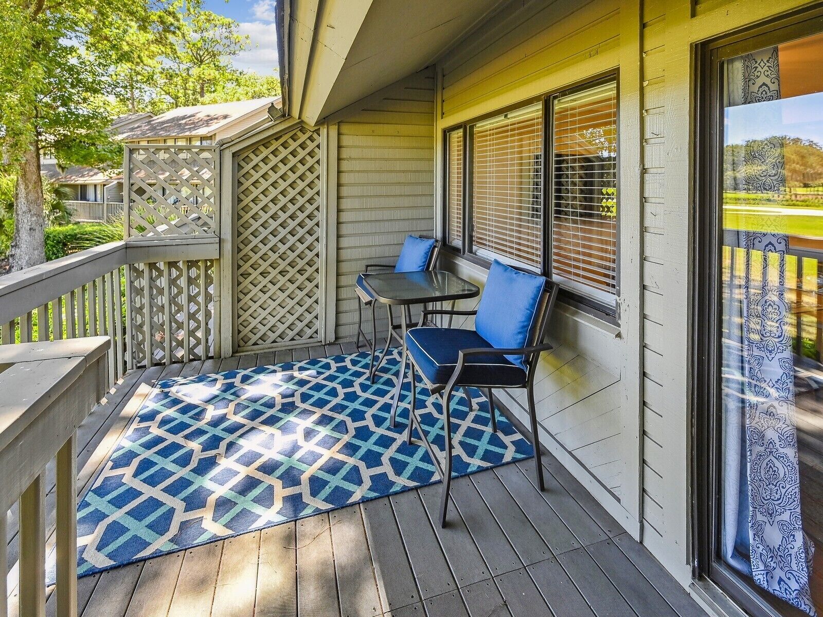 A covered porch with a patterned rug, two chairs, and a table.