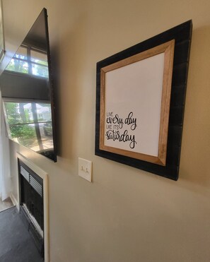 A framed motivational quote on a wall, a fireplace, and a window with a view of a house and street.