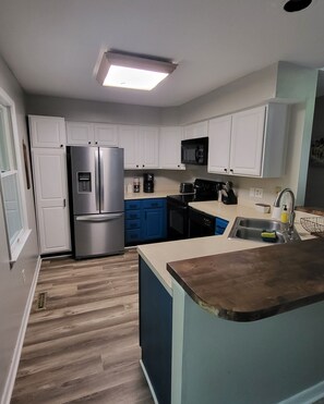 Una cocina moderna con gabinetes blancos, un refrigerador de acero inoxidable, un microondas y un lavamanos.