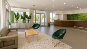 A spacious lobby with a reception desk, green chairs, a sofa, and a wooden table. - Oneway Savannah (Savannah)