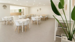 A spacious room with multiple white tables and chairs, a large plant, and decorative wall art. - Oneway Savannah (Savannah)