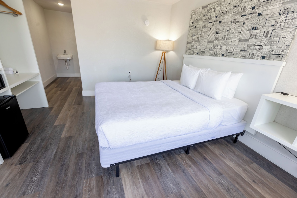 Ein ordentlich eingerichtetes Hotelzimmer mit einem Bett, einem Nachttisch, einer Lampe und einer Wand mit Stadtblick-Druck.