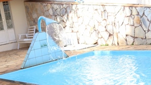 En swimmingpool med en stenvæg og et flisebelagt vandelement.