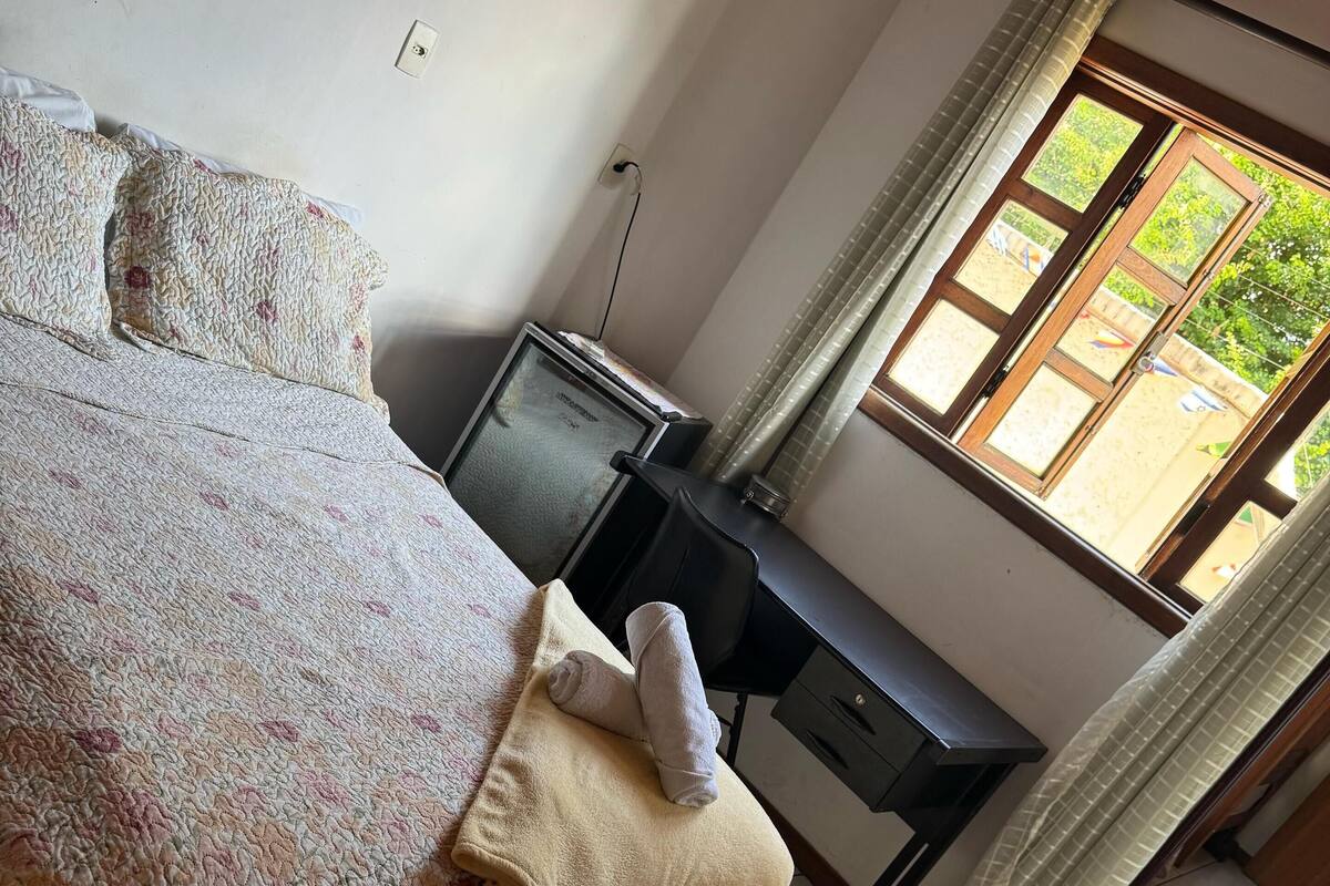 A bedroom with a bed, a desk, a television, and a window with curtains.