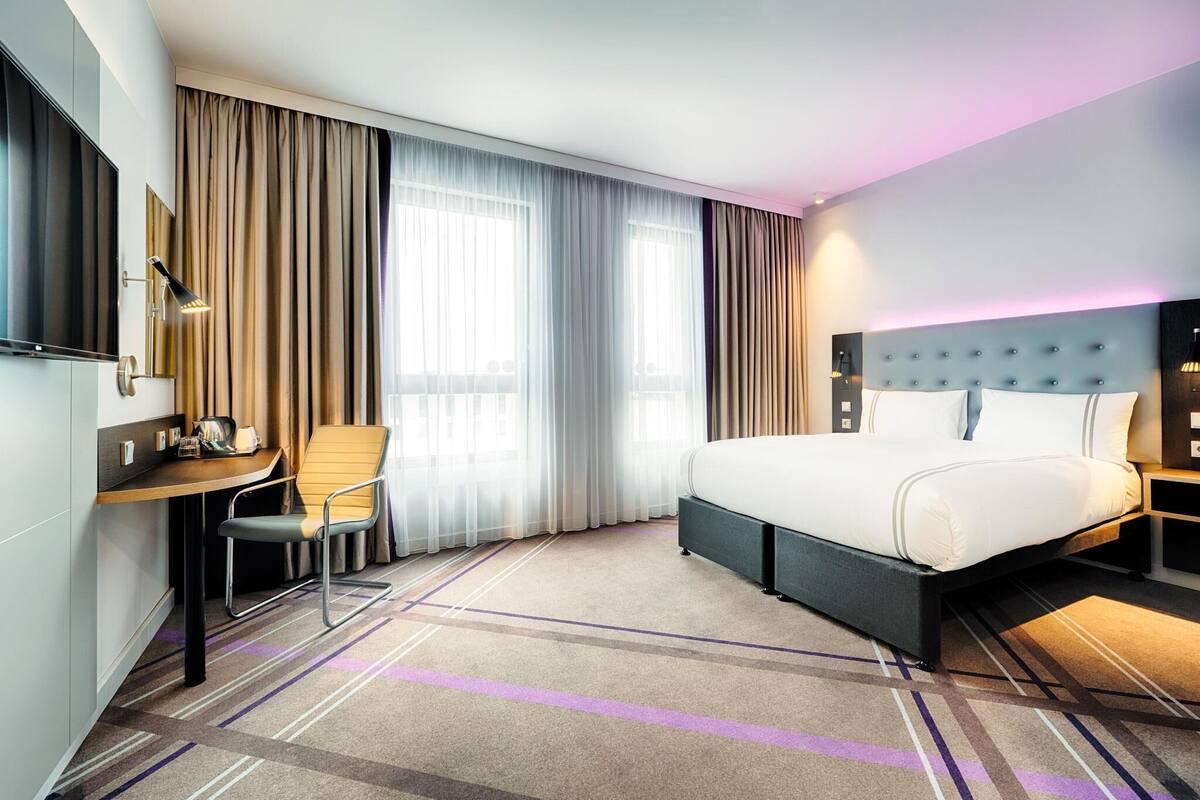 A hotel room with a bed, a desk, a chair, and a TV.