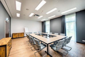 Ein Konferenzraum mit langem Tisch, Stühlen, einer Whiteboard-Tafel und einem Holzkasten.