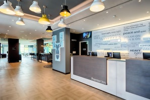 Ein Hotel-Empfangsbereich mit modernem Design, inklusive einer Rezeption, mehrerer Pendelleuchten und einer Wand mit Text und Bildern.