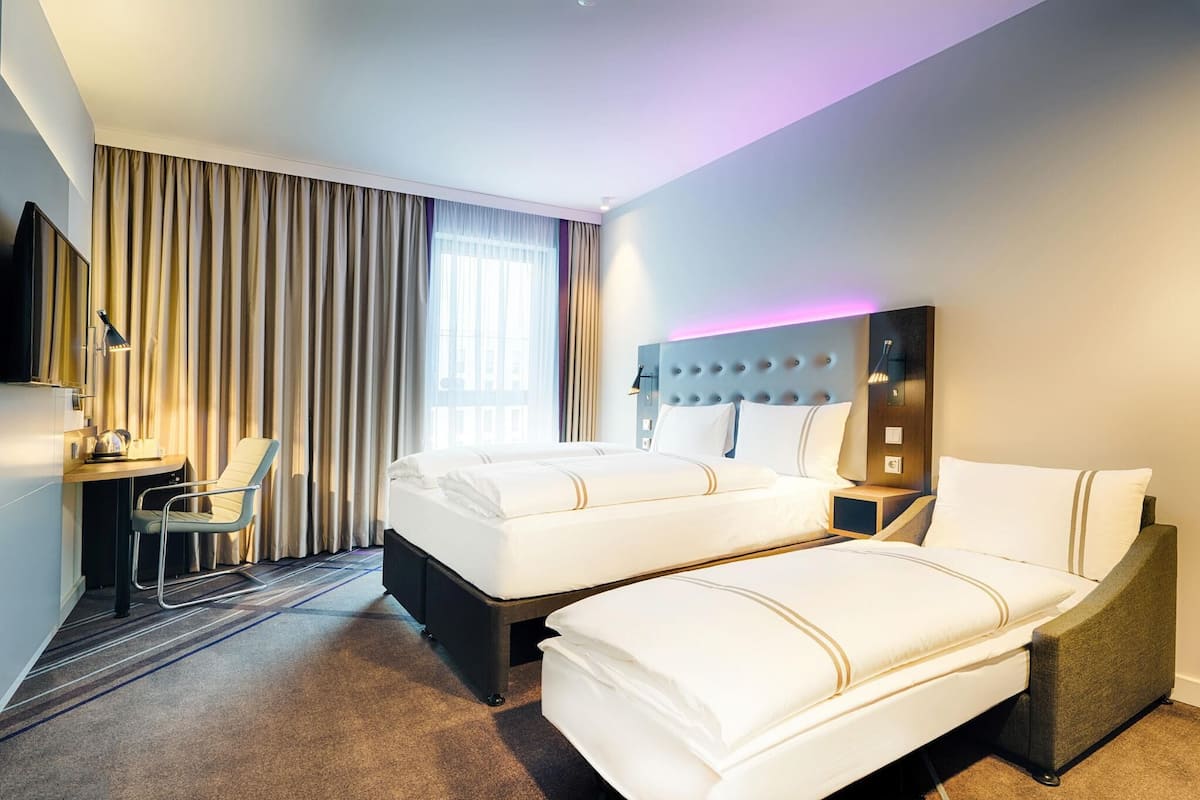 A hotel room with two beds, a desk, a chair, and a TV.