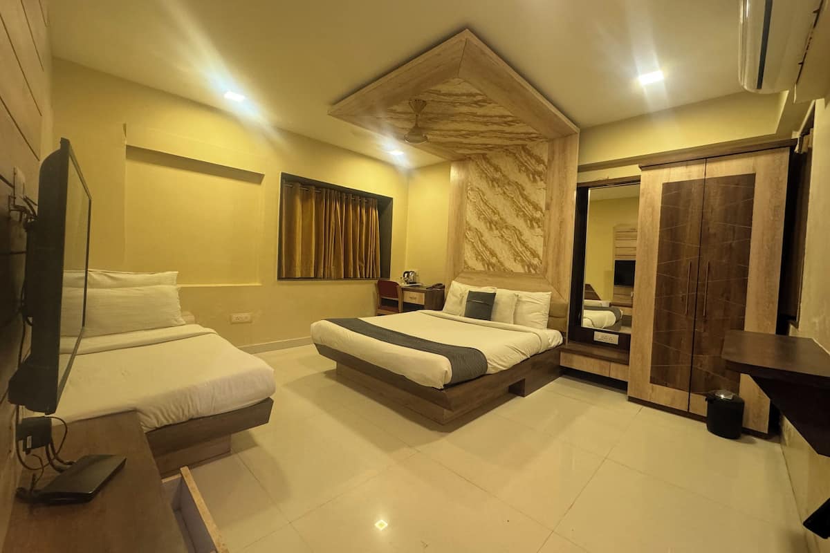 Habitación de hotel con dos camas individuales, una cama grande, cabecero de madera, un espejo, un armario y un televisor.