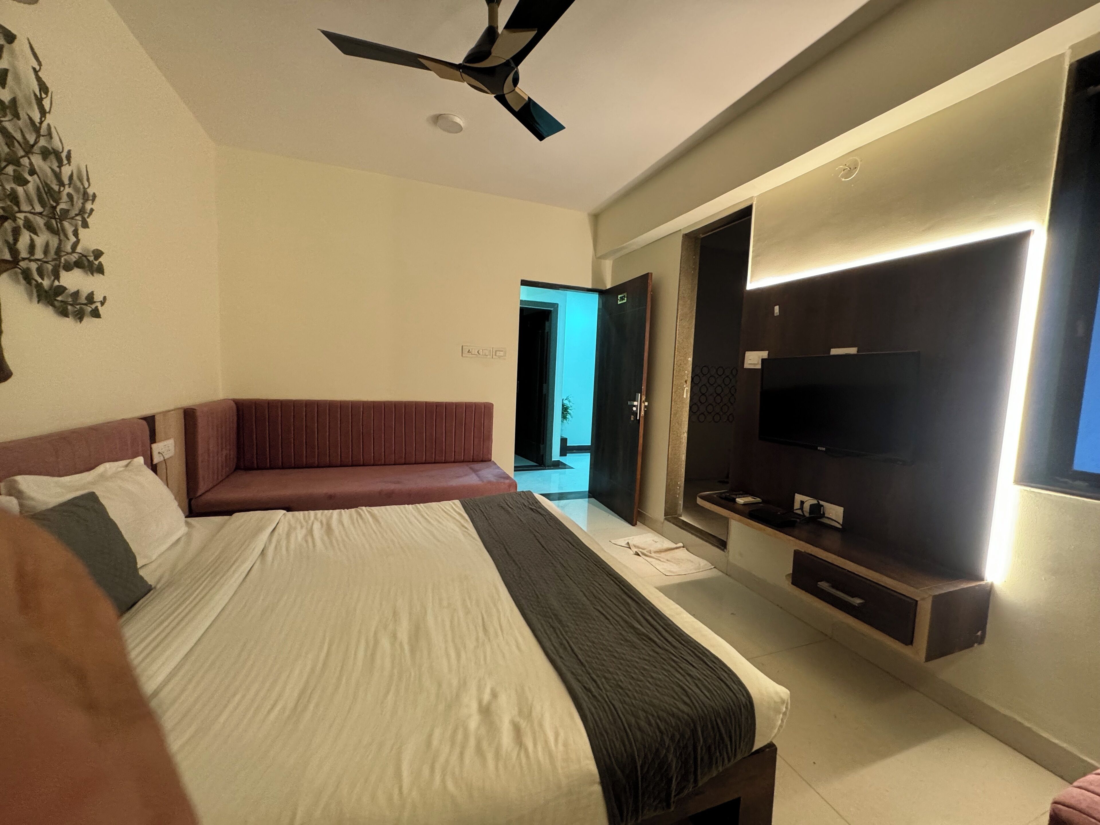 Un dormitorio con cama, ventilador de techo, televisor y puerta de baño.