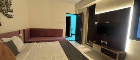 Un dormitorio con cama, ventilador de techo, televisor y puerta de baño.