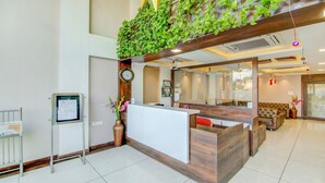 A reception area with a wooden reception desk, a clock, and a wall-mounted plant. - The Tripti Hotel (Indore)