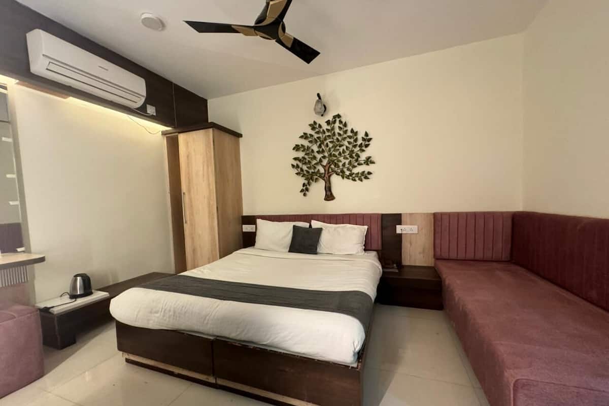 Un dormitorio moderno con una cama grande, un ventilador de techo, un equipo de aire acondicionado, una mesita de noche, un sofá rojo y un adorno de árbol montado en la pared.