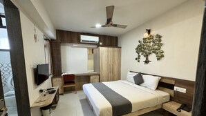 A bedroom with a bed, bedside table, nightstand, desk, chair, TV, wardrobe, and a ceiling fan. - The Tripti Hotel (Indore)