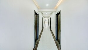 A long, narrow hallway with white walls and a tiled floor, leading to a door at the end. - The Tripti Hotel (Indore)