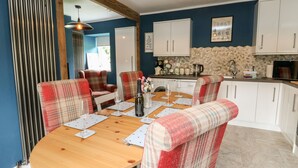 A dining area with a round wooden table, plaid chairs, and a kitchen in the background. - Ulla Dhu (Nethy Bridge)