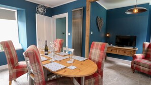 A dining area with a round wooden table, plaid chairs, and a television in the background. - Ulla Dhu (Nethy Bridge)