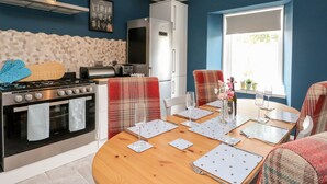 A modern kitchen with a gas stove, oven, and a built-in microwave. There is a dining area with a wooden table set for two, and a window providing natural light. - Ulla Dhu (Nethy Bridge)