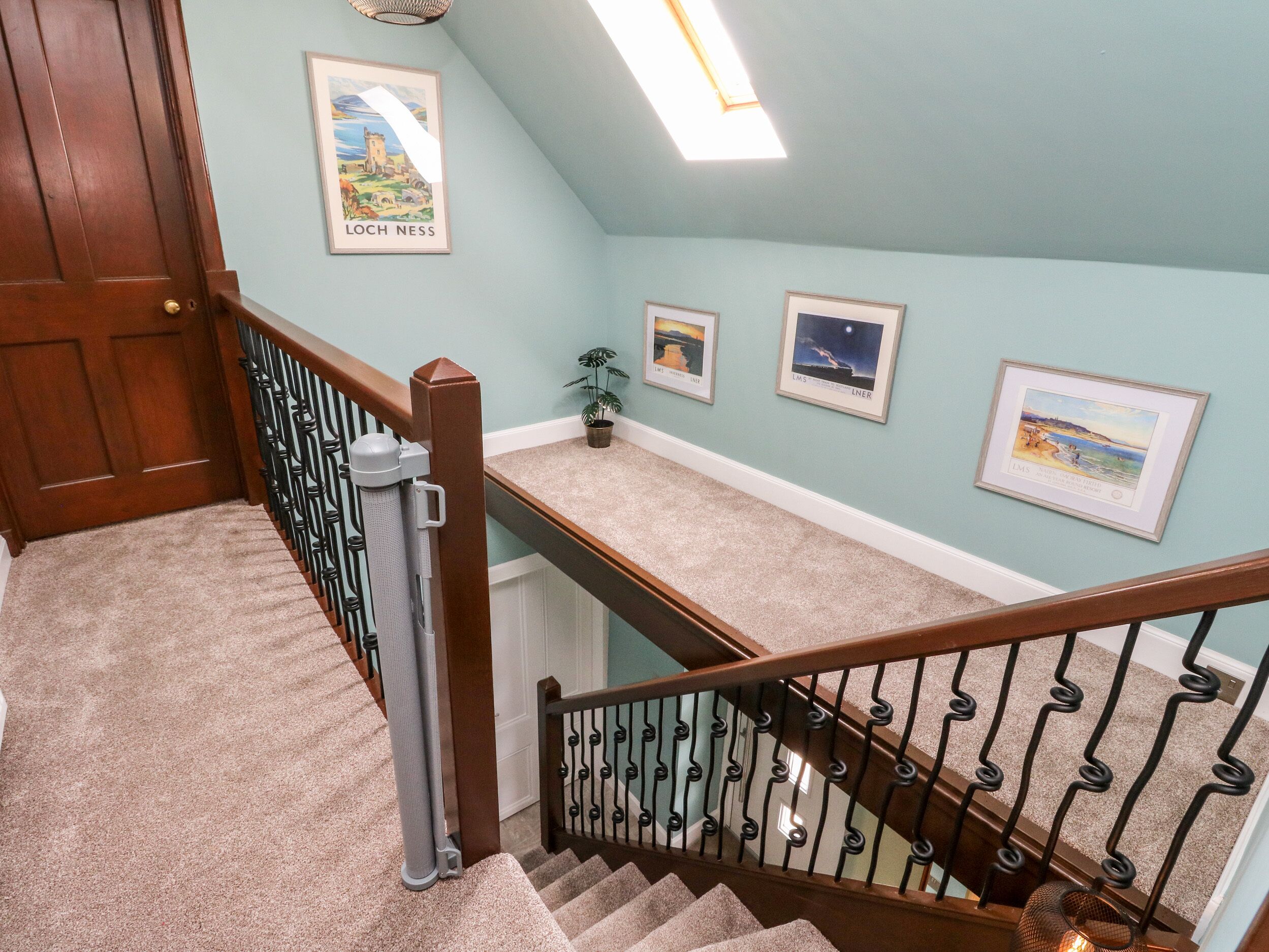 Eine Treppe mit Holzhandlauf und schwarzen Spindeln, mit Teppich belegten Stufen und einer hellblauen Wand mit gerahmten Bildern.