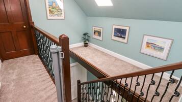 Eine Treppe mit Holzhandlauf und schwarzen Spindeln, mit Teppich belegten Stufen und einer hellblauen Wand mit gerahmten Bildern.