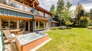 Une maison à deux étages avec un grand jardin, un jacuzzi et un patio aménagé avec du mobilier d’extérieur.