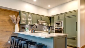 Une cuisine moderne avec des meubles de couleur verte, un grand îlot central doté de tabourets, un four à micro-ondes et une hotte de cuisine en acier inoxydable.