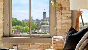 Una habitación con un ventanal grande, vistas a un paisaje urbano, una lámpara y una cama con almohadas.