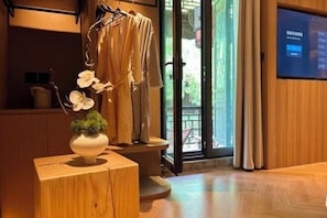 A room with a wooden floor, a small wooden table with a vase of flowers, a hanging garment, and a sliding glass door leading to an outdoor area. - Huajiadi Inn (Taierzhuang Ancient City Scenic Area) (Zaozhuang)