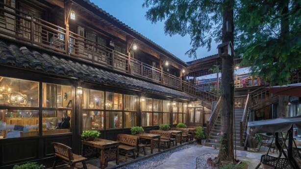 Un edificio tradicional de madera con un área de estar al aire libre techada, un camino de piedra y una escalera que lleva a un nivel superior.