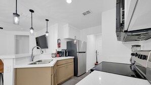 Eine moderne Küche mit weißen Arbeitsplatten, einem Edelstahl-Kühlschrank und Pendelleuchten.