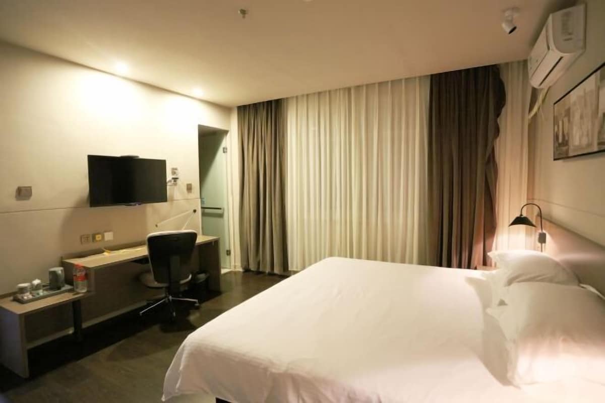 Habitación de hotel con cama, escritorio, silla, televisor y cortinas.