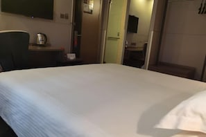 Una habitación de hotel con una cama grande, un escritorio con un hervidor y un televisor en la pared.