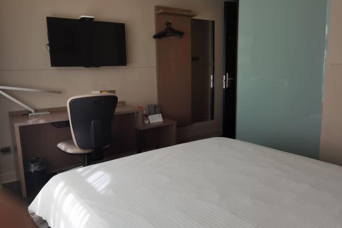 Una habitación de hotel con cama, escritorio con silla, televisión y armario.